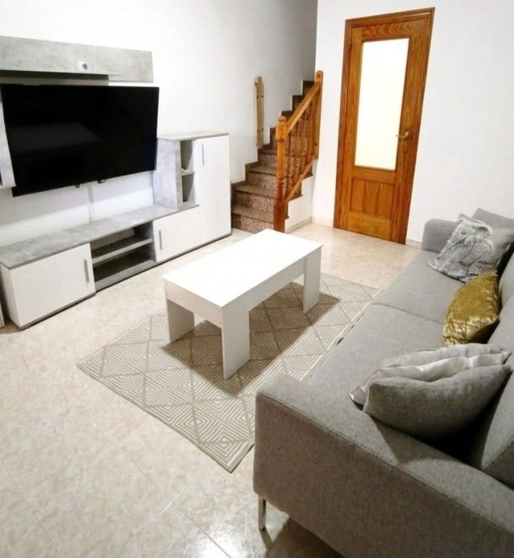 Modernt vardagsrum med soffa, TV, soffbord och trappa.