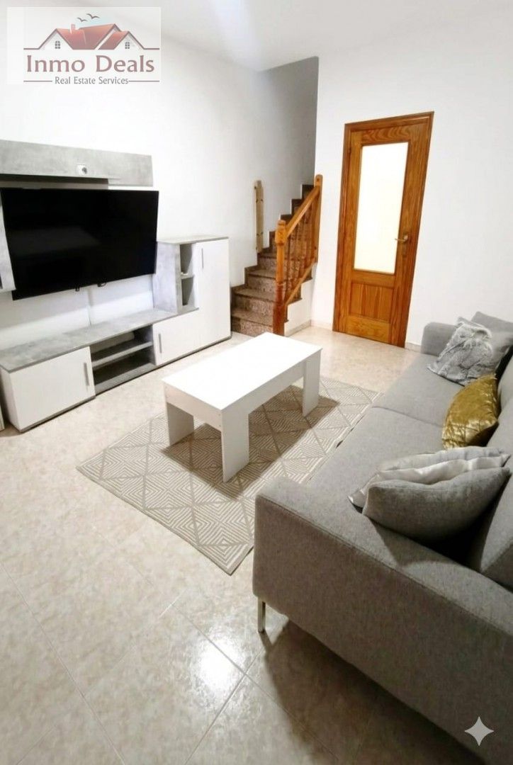 Modernt vardagsrum med soffa, TV, soffbord och trappa.