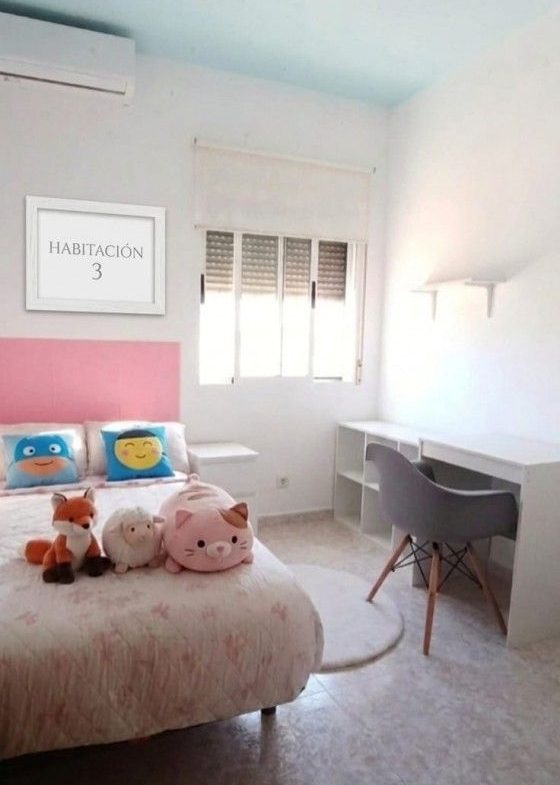 Ljust sovrum med rosa säng, skrivbord, fönster och luftkonditionering.