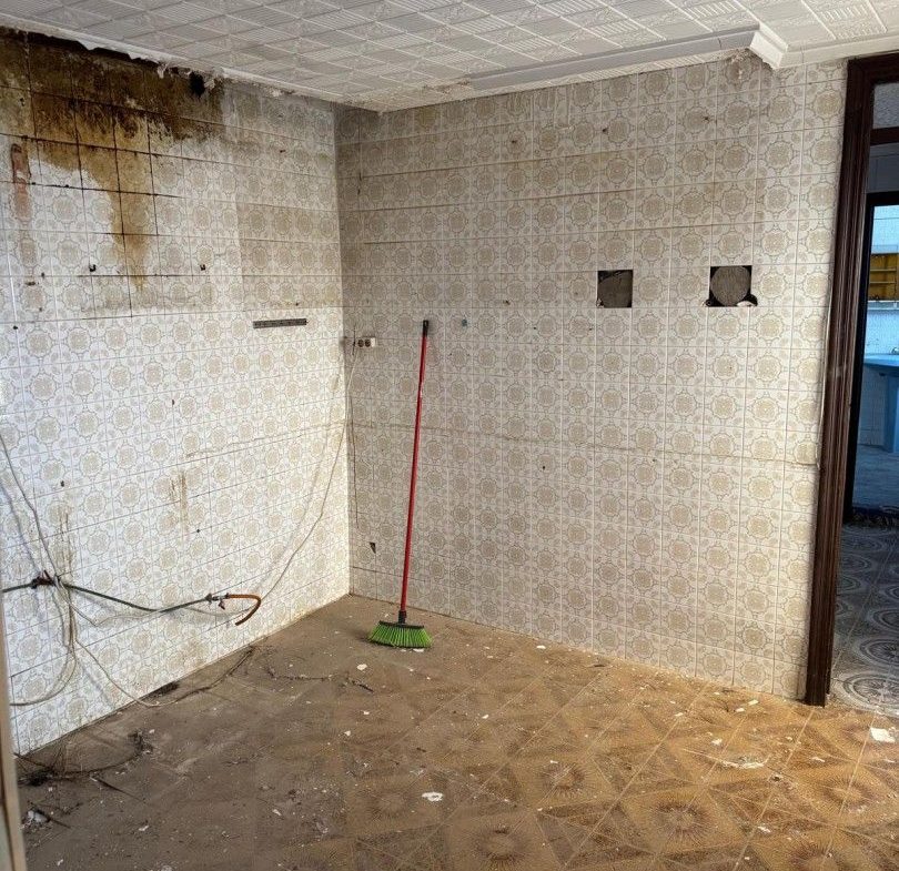 Smutsigt, förfallet kök med kakel och fuktskada, redo för renovering.
