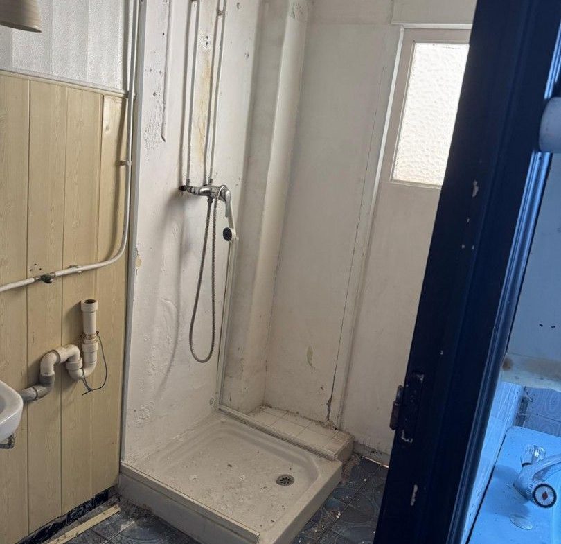 Gammalt, smutsigt badrum med dusch, stort renoveringsbehov.