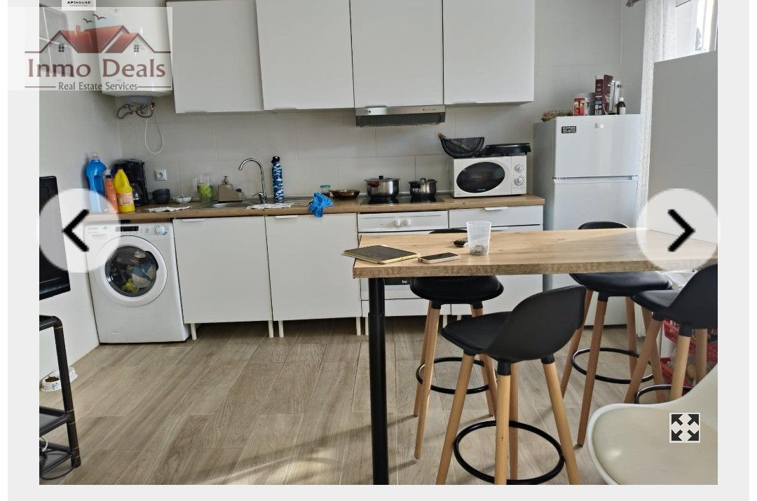 Modernt kök med tvättmaskin, matplats, vita skåp, träbänkskiva.