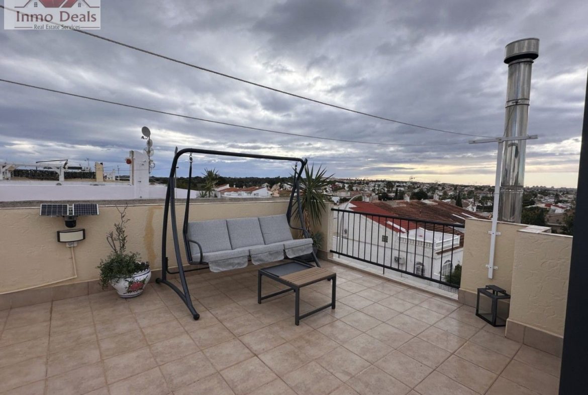 Rymlig takterrass med gungssoffa och stadsvy under molnig himmel.