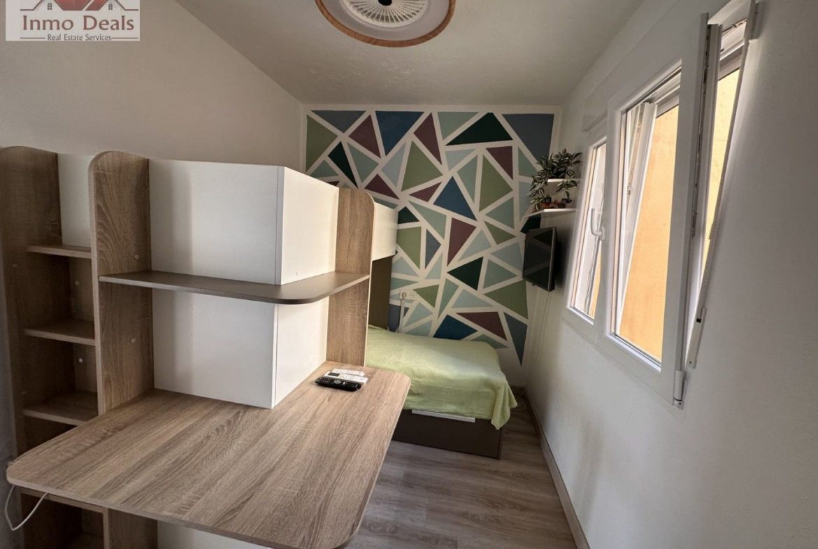 Modernt sovrum med säng, skrivbord, geometrisk vägg och fönster.