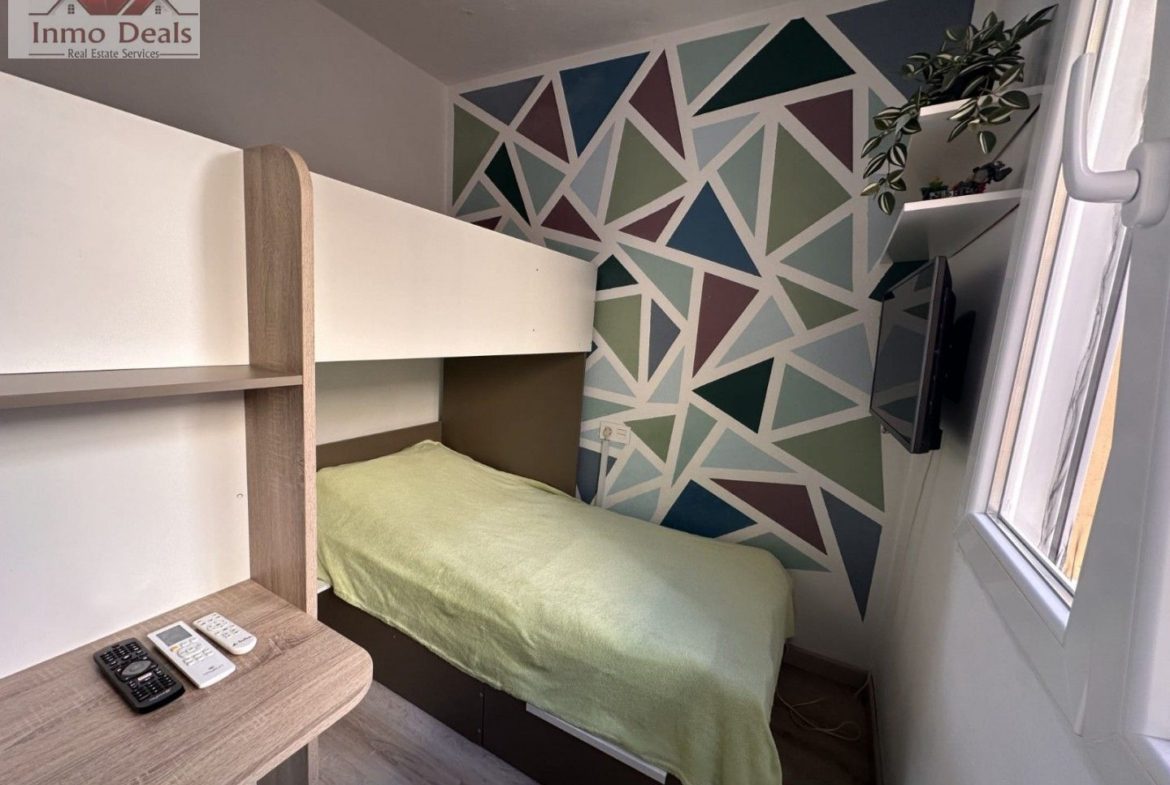 Litet sovrum med våningssäng och färgglad geometrisk vägg.