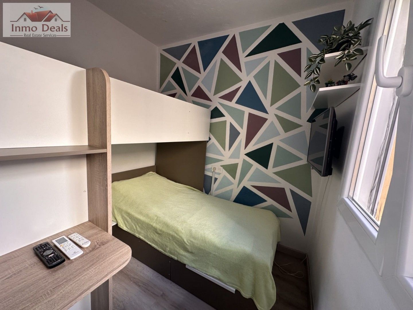Litet sovrum med våningssäng och färgglad geometrisk vägg.